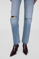 Jean celeste de tiro alto, corte recto y ajustado al tobillo, con roturas en las rodillas y terminación desflecada.