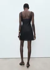 Vestido corto negro de corte ajustado, sin mangas y con cuello redondo. Presenta detalle drapeado en la falda.