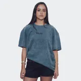 Remera de manga corta, corte oversize, color azul con efecto acid wash o distorsión. Presenta un pequeño texto bordado o estampado en el pecho.
