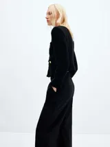 Chaqueta negra de tweed con cuello redondo, cierre frontal con botones dorados, bolsillos de parche y flecos en el ruedo.