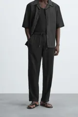 Pantalón negro de corte amplio, con textura acanalada, cintura elástica ajustable con cordón, bolsillos laterales y traseros de vivo.