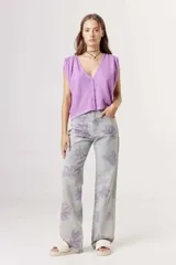 Jeans de corte recto con estampado floral en tonos lilas sobre fondo gris claro.