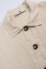Campera color crema estilo sobre camisa hecha en lino premium con cuello clásico, cierre con botones marrones, dos bolsillos de parche inferiores y un bolsillo de parche superior.