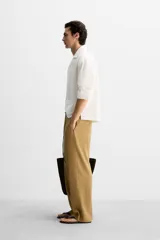 Camisa blanca de corte relaxed fit confeccionada en tejido de algodón y lino. Tiene cuello bowling, manga larga con puños abotonados, jaretas en el delantero, bolsillos de parche en pecho y cadera, bajo con aberturas laterales y cierre frontal con botones.