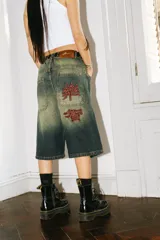 Bermuda baggy de jean con lavado verde, bordado en negro y rojo, cierre y botón personalizado, corte amplio y bolsillos grandes.