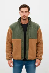 Campera de estilo outdoor confeccionada en tejido tipo corderito, con paneles en contraste de color verde y marrón. Presenta cierre frontal con botones a presión, cuello alto y bolsillo vertical con cierre en el pecho.