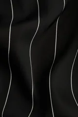 Pantalón holgado negro con finas rayas verticales blancas, tiro alto, cintura elástica, bolsillos laterales y ribete decorativo en los bajos.