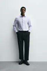 Camisa celeste a rayas verticales blancas, de corte recto, con cuello italiano abierto, mangas largas con puños abotonados y cierre frontal con botones.