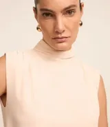 Blusa color crema de poliéster satinado, con cuello alto, sin mangas y botón en la nuca.
