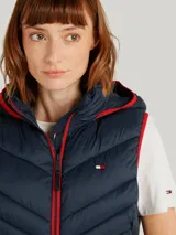 Chaleco acolchado azul marino con capucha ajustable con cordones y cierre de cremallera frontal. Bolsillos laterales con cremallera y logo de Tommy Hilfiger bordado en el pecho. Detalles distintivos de Tommy Hilfiger en el ruedo.