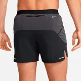 Short deportivo negro con logo Nike Trail estampado en blanco, cintura elástica con cordón ajustable y paneles laterales en gris.