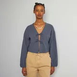 Blusa azul de algodón con textura arrugada, escote en V con lazos y mangas largas abullonadas.
