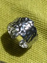 Anillo plateado regulable de acero inoxidable con forma irregular y superficie texturizada.