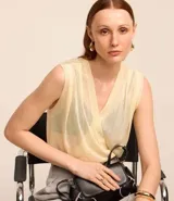 Body color crema de retilínea fina, con escote cruzado en pico, sin mangas y con detalle de pliegues en los hombros.