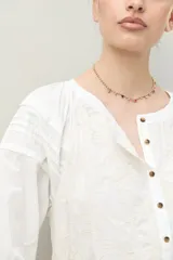 Vestido corto blanco de algodón con bordado floral en relieve, escote redondo con abotonadura frontal y mangas amplias.