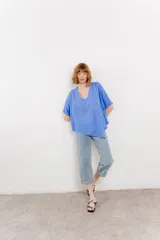 Blusa color naranja confeccionada en 100% lino, con escote en V, mangas cortas con vuelta y silueta amplia. Presenta terminación asimétrica y fila de botones decorativos en uno de los hombros.