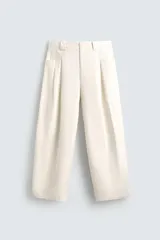 Pantalón color crema de corte ancho, con pliegues frontales, bolsillos laterales y traseros.