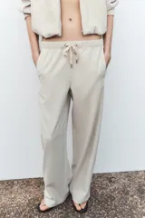 Pantalón de tiro alto color hueso, con bolsillos delanteros y traseros, cintura elástica ajustable con cordones y corte ancho.