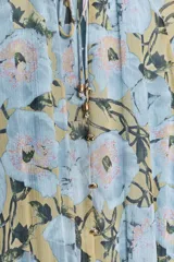 Vestido largo con estampado floral en tonos celeste, amarillo y marrón. Tiene cuello redondo con volantes y lazada, escote pico, manga larga con puño elástico con volantes, forro interior y cierre frontal con botones.