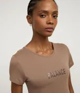 Remera deportiva femenina de manga corta y cuello redondo, color marrón topo, confeccionada en poliamida con tecnología Dry. Presenta la palabra "Balance" en relieve en el pecho.