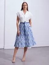 Vestido midi camisero de algodón con estampado floral en tonos azules y blancos. Tiene cuello solapado, cierre frontal con botones, manga corta, cintura elastizada con lazo de ajuste y bolsillos laterales.