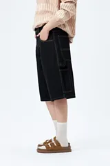 Bermuda carpenter de denim negro, corte relajado y largo a la rodilla, con costuras visibles y múltiples bolsillos funcionales.