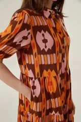Vestido midi con estampado abstracto en tonos marrón, naranja y rosa. Tiene cuello camisero, mangas cortas abullonadas y falda escalonada con volantes.