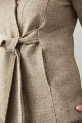 Chaqueta corta color beige, entallada, con escote en V, manga larga y cierre frontal con lazo fijo. Confeccionada en lana fina sin teñir, con bolsillos escondidos y terminaciones enviadas. Hecha 100% en Uruguay.
