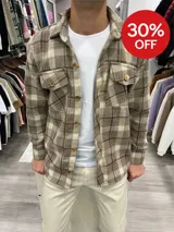 Sobrecamisa de paño a cuadros color tostado, con cuello clásico, cierre frontal con botones de madera, dos bolsillos de parche con solapa abotonada en el pecho y puños abotonados.