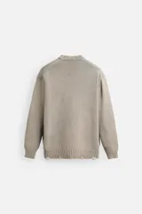 Jersey de punto color beige, de corte holgado, con cuello redondo y manga larga. Tiene efecto lavado y rotos en toda la prenda.