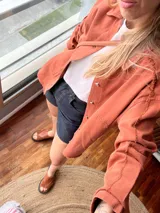 Sobre camisa color ladrillo con cuello camisero, cierre frontal con botones metálicos y bolsillos de parche en el pecho.