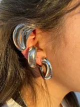 Aros tipo cuff plateados, gruesos y con diseño moderno.