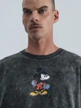 Remera negra con efecto nevado, corte oversize y estampado de Mickey Mouse sobre una patineta.