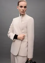 Blazer color beige con solapas de muesca, cierre frontal con un botón, hombros estructurados, corte entallado, forro interior y dos bolsillos de ribete en la parte delantera.