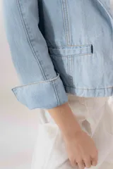 Blazer celeste de denim 100% algodón, entallado y corto a la cadera, con cuello y solapa amplios, mini bolsillos delanteros y bordado con el logo de la marca en el interior del puño.