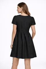 Vestido corto negro de broderie, con mangas cortas abullonadas y escote en V. Presenta un corte imperio con frunce en la cintura y falda acampanada.