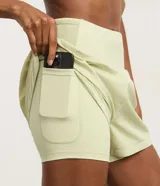 Bermuda deportiva femenina de microfibra color amarillo claro, con diseño de doble capa: un short interno ajustado y una capa externa suelta con bajo redondeado. Posee cintura alta.