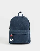 Mochila azul de denim con bolsillo frontal con cierre y tirador con charms decorativos. Tiene correas regulables, manija superior y cierre superior.