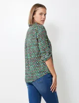 Blusa de gasa con estampado geométrico en tonos verdes, azules y morados. Presenta cuello con solapa, escote en V con botones y mangas largas que se pueden remangar y sujetar con presilla.
