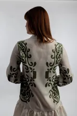 Vestido corto color crema con estampado de motivos geométricos en verde. Tiene cuello mao con lazo y borlas, mangas 3/4 y falda con volantes.