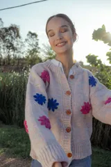 Cardigan tejido en lana color rosa claro con flores bordadas a mano en colores fucsia y azul. Tiene cuello redondo, cierre frontal con botones de madera y mangas largas.