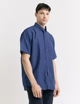 Camisa de manga corta azul con estampado de lunares blancos, cuello abotonado y bolsillo en el pecho.