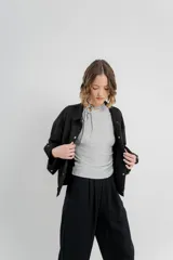 Chaqueta color beige de corte recto, estilo camisa, confeccionada en gamuza con elastano. Presenta cuello camisero, cierre frontal con botones metálicos, bolsillos grandes en el frente y charreteras en los hombros.