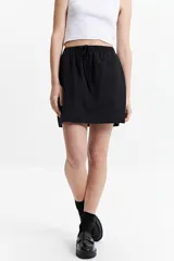 Minifalda negra de algodón con cintura elastizada con lazo regulable y bolsillos laterales.