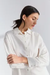 Conjunto de pijama blanco de lino y viscosa, compuesto por un corpiño de encaje, una camisa de mangas largas y un pantalón capri con lazo en la cintura.