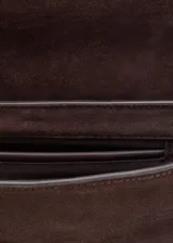 Bolso de hombro rectangular de piel de serraje color marrón oscuro, con solapa curva y cierre metálico central. Presenta costuras decorativas blancas en los laterales y una correa fina de hombro.