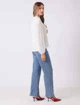 Blusa blanca de gasa plisada con encaje calado en el cuello y el pecho. Cuello a la base fruncido, manga larga con puño elastizado y espalda lisa con abertura tipo gota y botón.