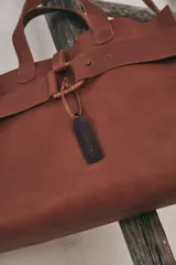 Bolso tote de cuero color marrón con correa larga ajustable y cierre con hebilla.