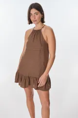 Vestido corto color beige, con escote halter, tirantes finos y falda con volados.