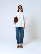 Blusa blanca de mangas largas con cuello alto fruncido y puños elásticos.